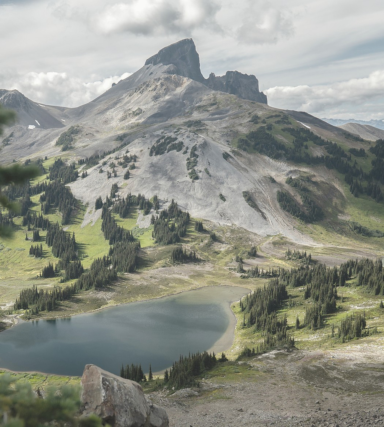 A rugged mountain peak rising above a small alpine lake and evergreen forest